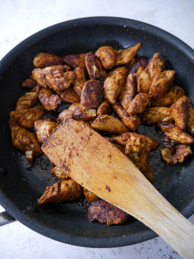 A non stick pan filled with cooked spice coated pieces of chicken breast.