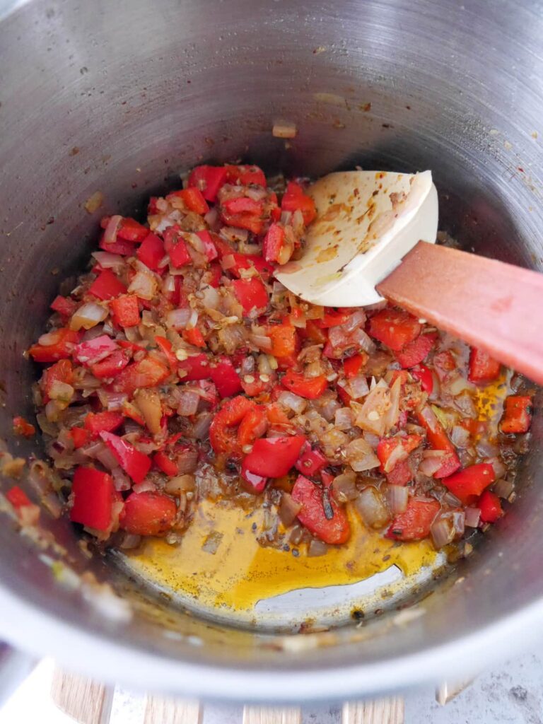 A saucepan of sauteed and spiced shallot, red bell pepper and garlic.