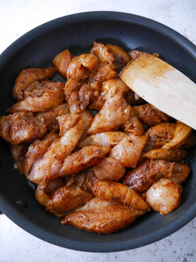 A non stick pan filled with uncooked spice coated pieces of chicken breast.