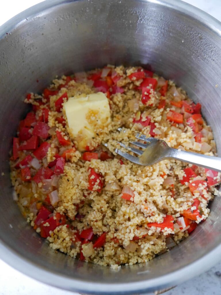 A pan of cooked couscous with butter being forked through.
