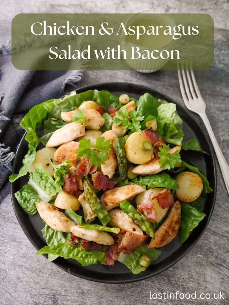 Pinnable image with recipe title and a black plate topped with a salad of lettuce leaves, sauteed chicken, asparagus, new potatoes and bacon.