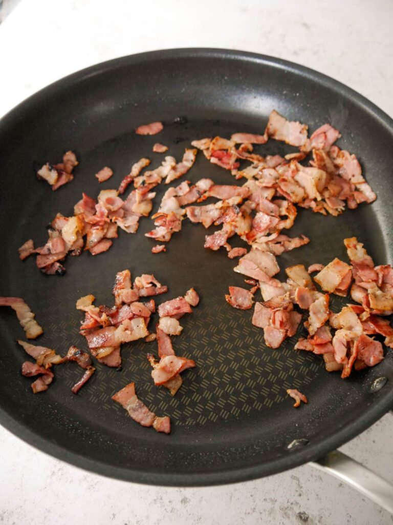 A nonstick frying pan filled with sauteed bacon pieces.