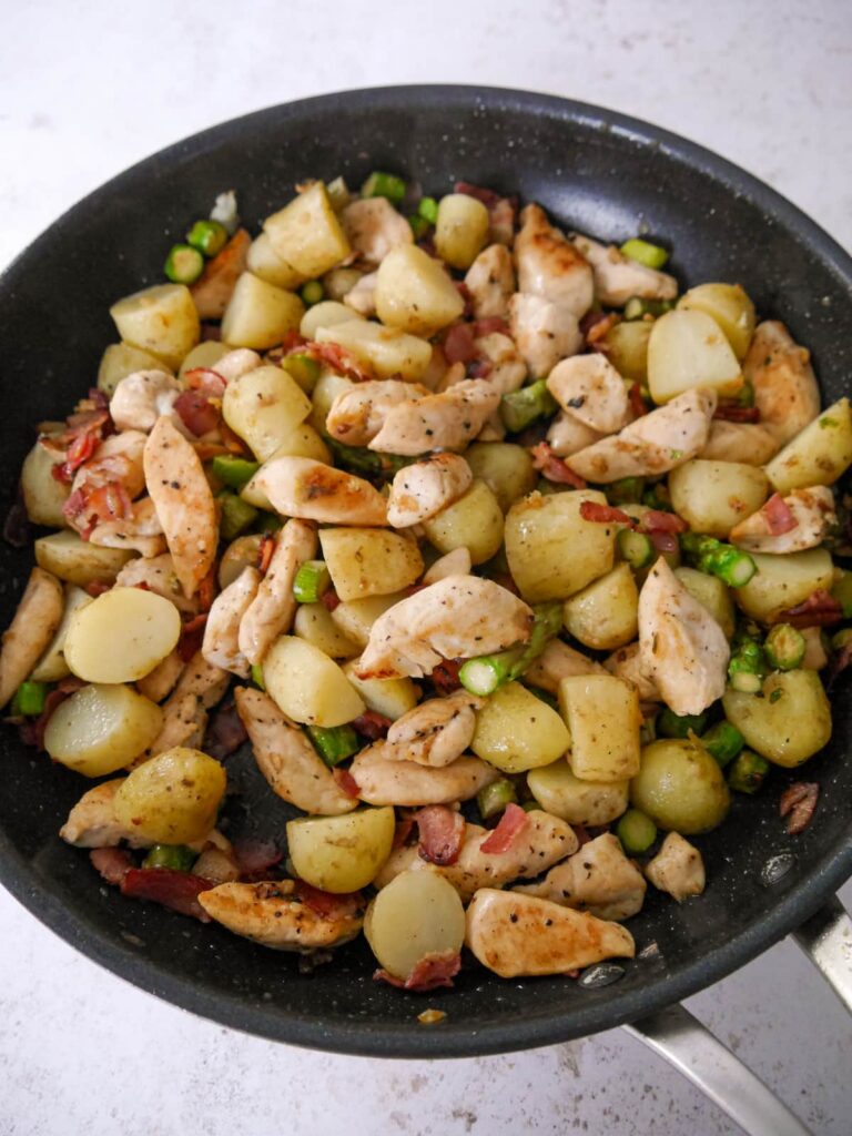A nonstick frying pan filled with cooked chicken, asparagus, bacon and new potatoes.