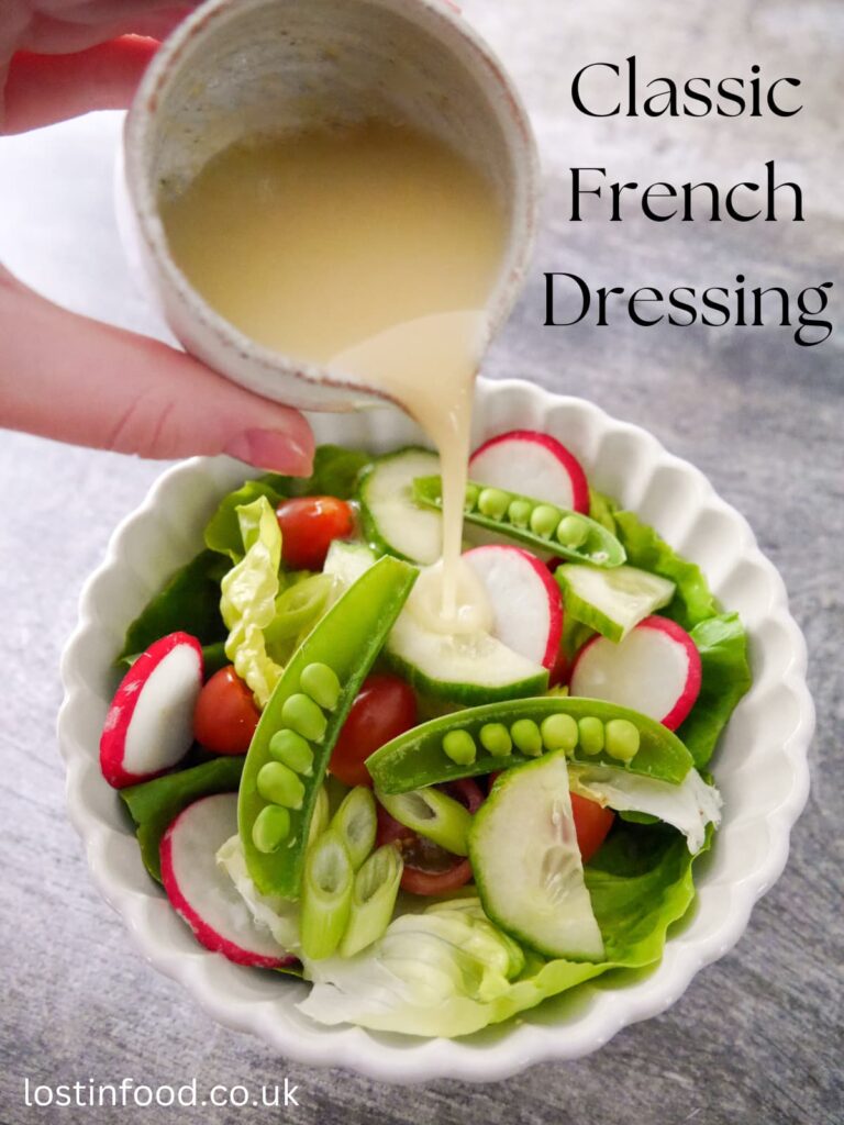 Pinnable image with recipe title and a small jug of French dressing being poured over a white bowl filled with salad of lettuce, radish, tomato, cucumber, spring onions and sugar snap peas.