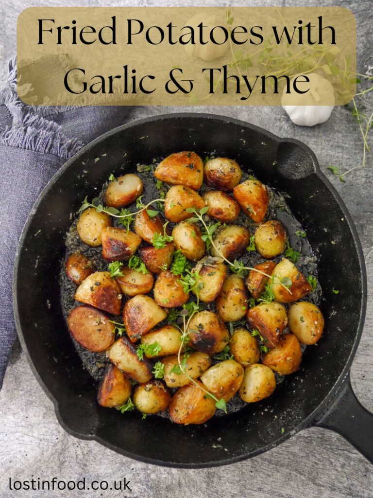 Pinnable image with recipe title and a cast iron skillet filled with fried potatoes in a garlic and thyme butter, garnished with fresh herbs.