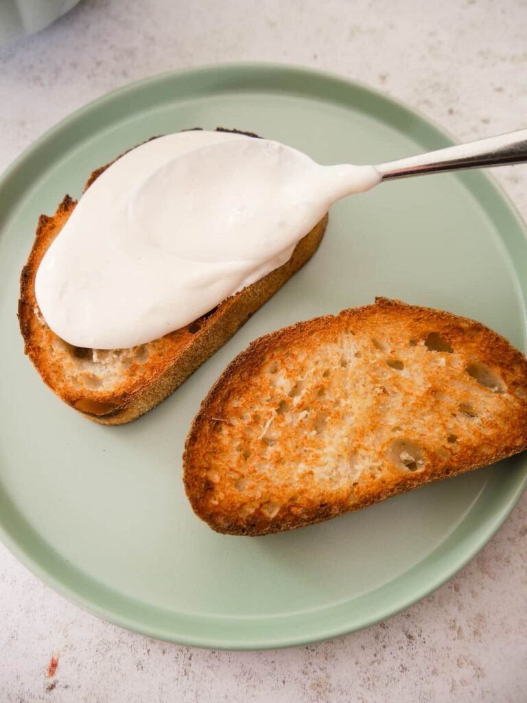 Two slices of sourdough toast being spread with whipped creme fraiche.