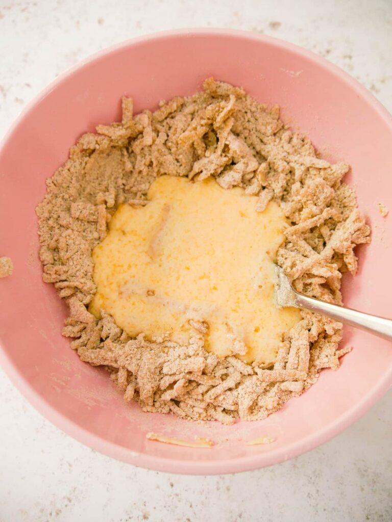 A pink mixing bowl filled with scone dry ingredients, mixed with apple and added egg and buttermilk.