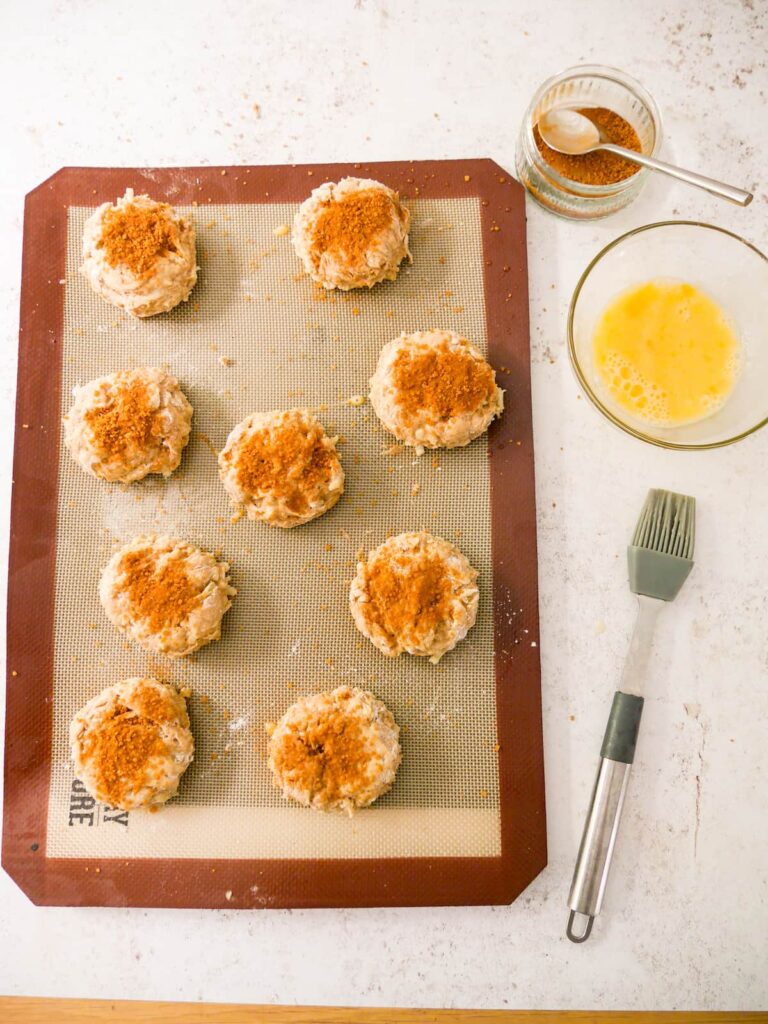 Apple and cinnamon scones, topped with egg wash and cinnamon sugar, set on a baking sheet topped with a silicone liner.