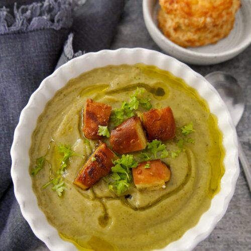 A bowl of broccoli and courgette soup topped with fresh parsley and croutons, with a cheese scone served alongside.