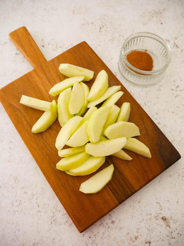 A wooden board topped with pared, cored and sliced apple.