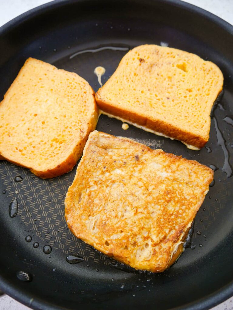 A large non stick frying pan with 3 slices of French toast being cooked.