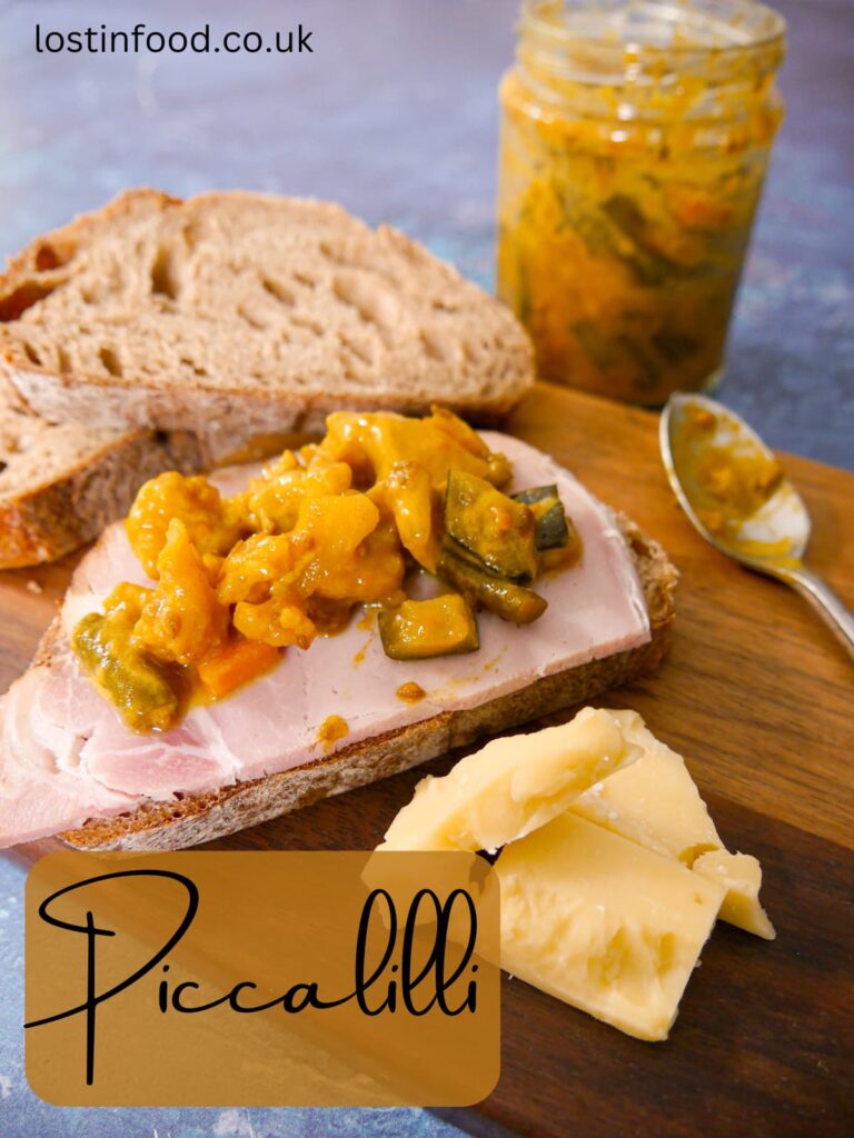 Pinnable image with recipe title and a wooden board topped with slices of sourdough bread, topped with ham and piccalilli with cheese, and a jar of piccalilli set alongside.