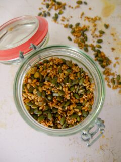 Kilner jar filled with a mixture of seasoned, roasted seeds, including pumpkin, sunflower, sesame and golden flax seeds.