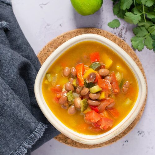 A bowl of spicy bean soup with lime and coriander leaf set alongside.