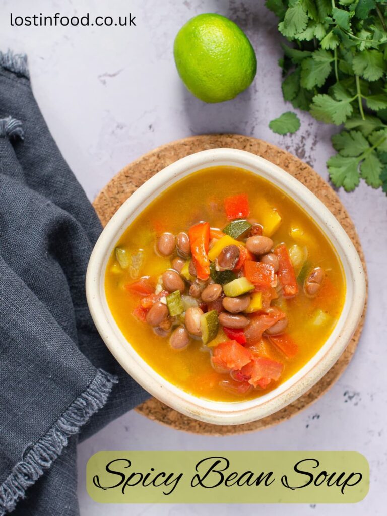 Pinnable image and recipe title with image of a bowl of spicy bean soup with lime and coriander leaf set alongside.