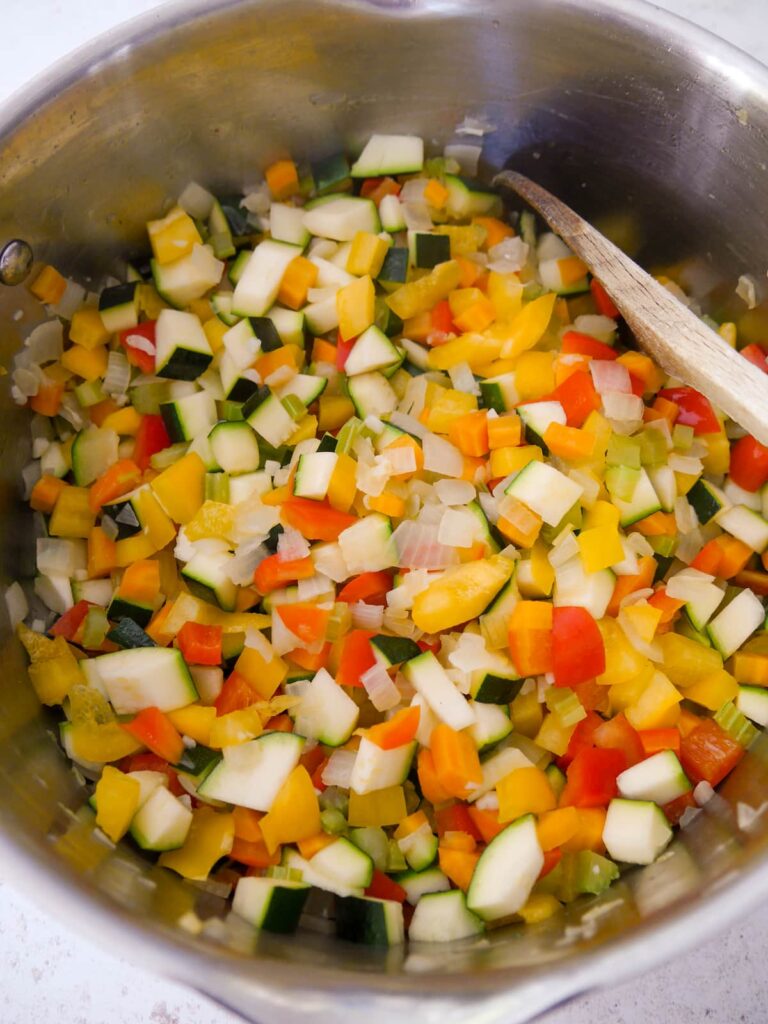 A large saucepan filled with sauteed onion, carrot and celery with added diced bell pepper and courgette.