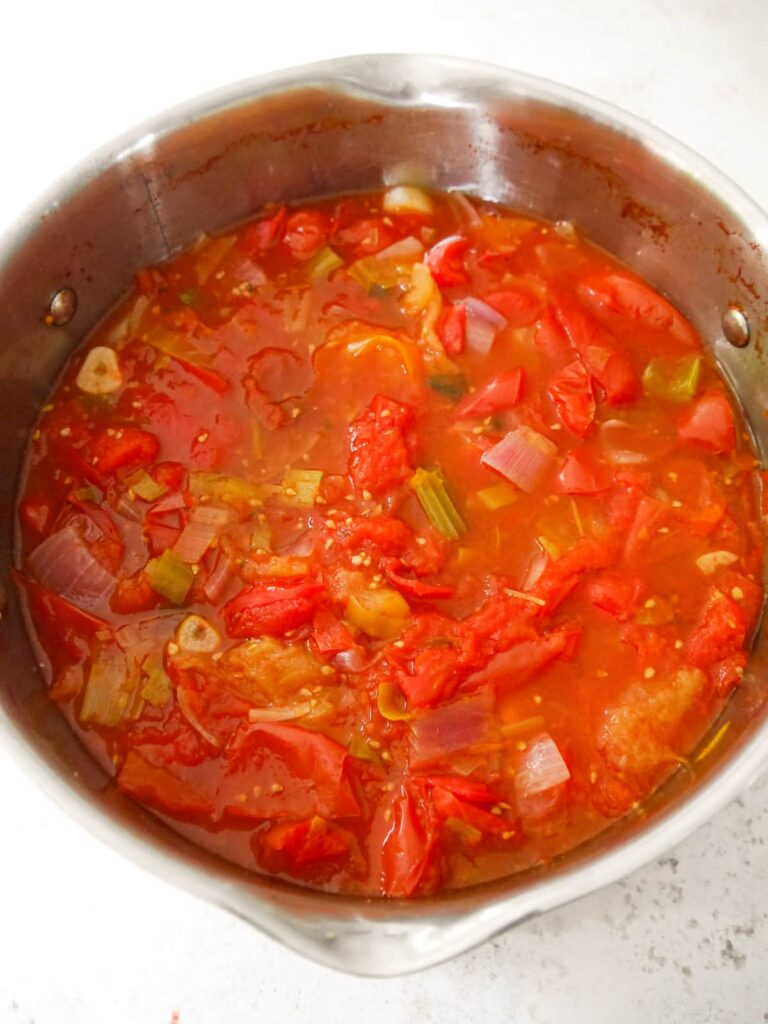 A large saucepan filled with cooked tomatoes, vegetables and herbs.