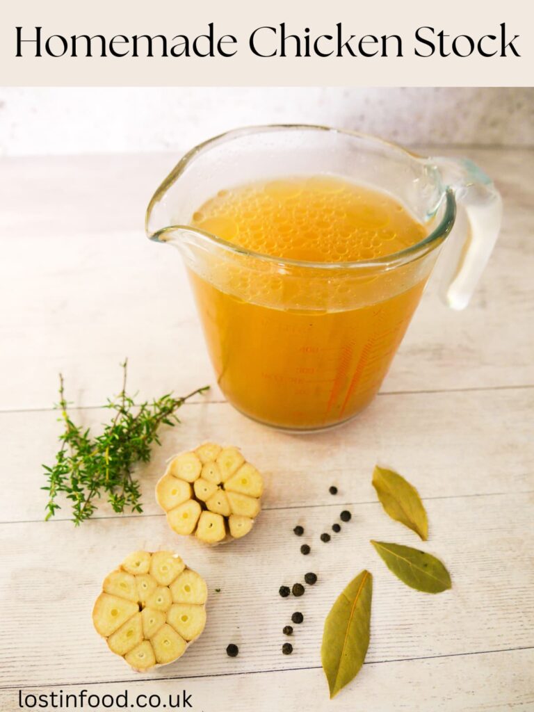 Pinnable image with recipe title and a jug of homemade chicken stock with fresh thyme, garlic, black peppercorns and dried bay leaves set alongside.