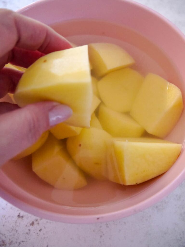 A bowl of peeled and cut potatoes soaking in water.