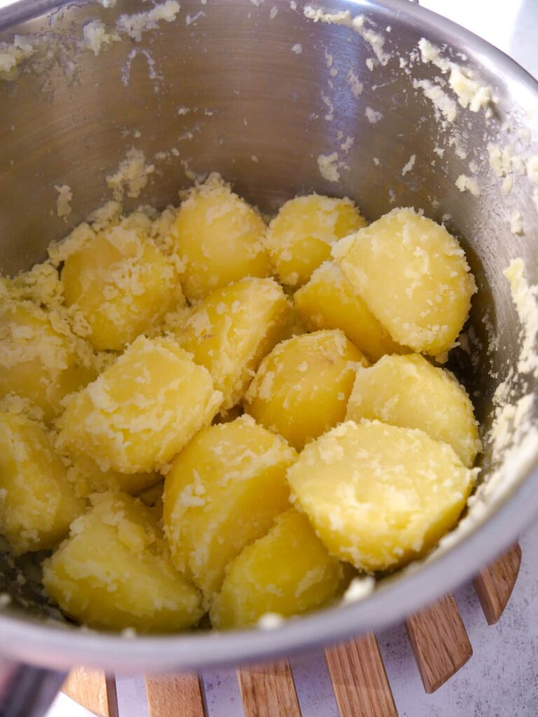 A pan of par boiled potatoes that have been roughed around the outside.