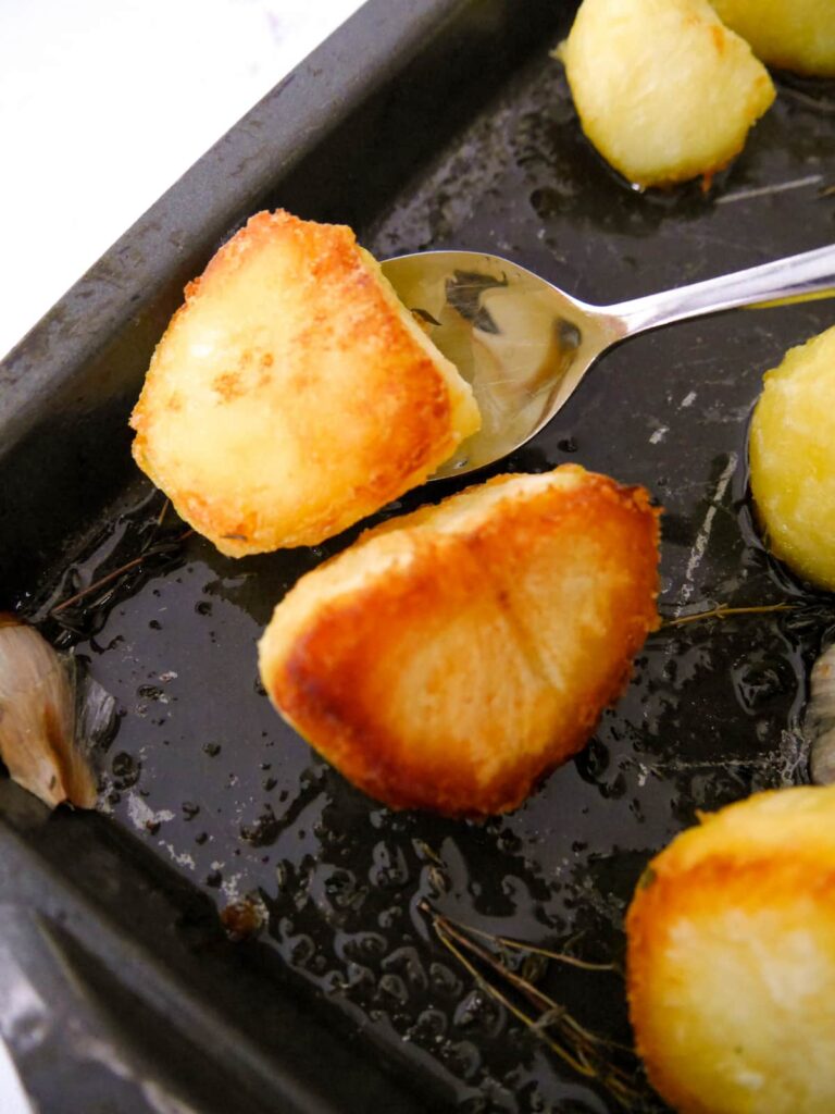 A roasting dish of part roasted potatoes being turned over mid way through the cook.