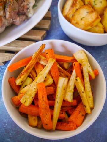 A bowl of honey roasted carrots and parsnips with roast potatoes and turkey set alongside.