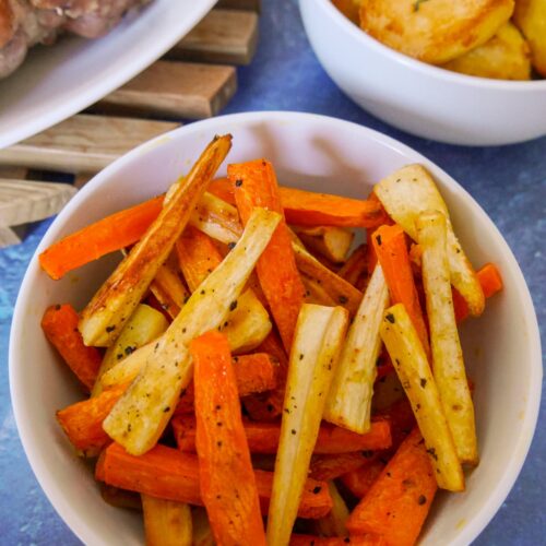 A bowl of honey roasted carrots and parsnips with roast potatoes and turkey set alongside.