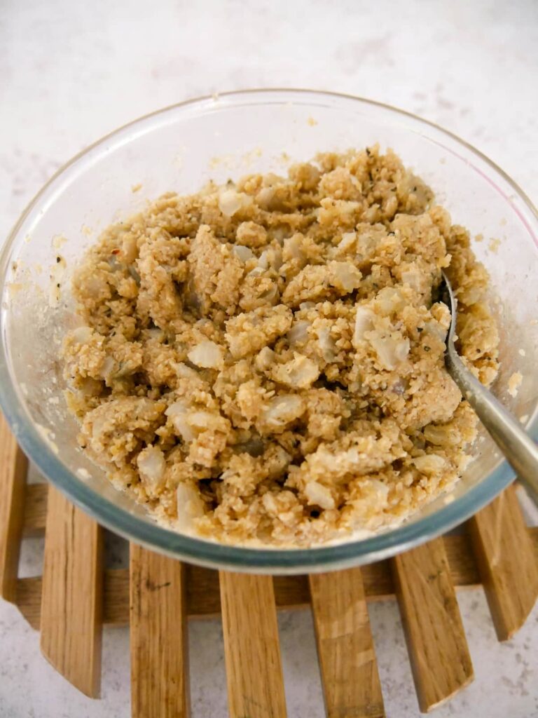 A bowl of part cooked oatmeal stuffing being stirred with a spoon.