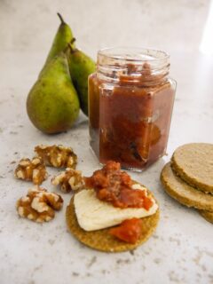 A jar of pear and walnut chutney, with pears, walnuts and cheese and chutney topped oatcakes set alongside.