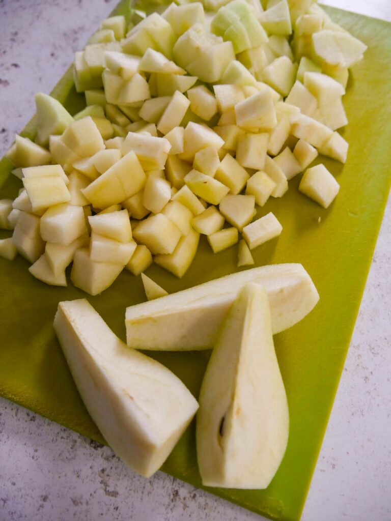 A chopping board with chopped apples and pears.