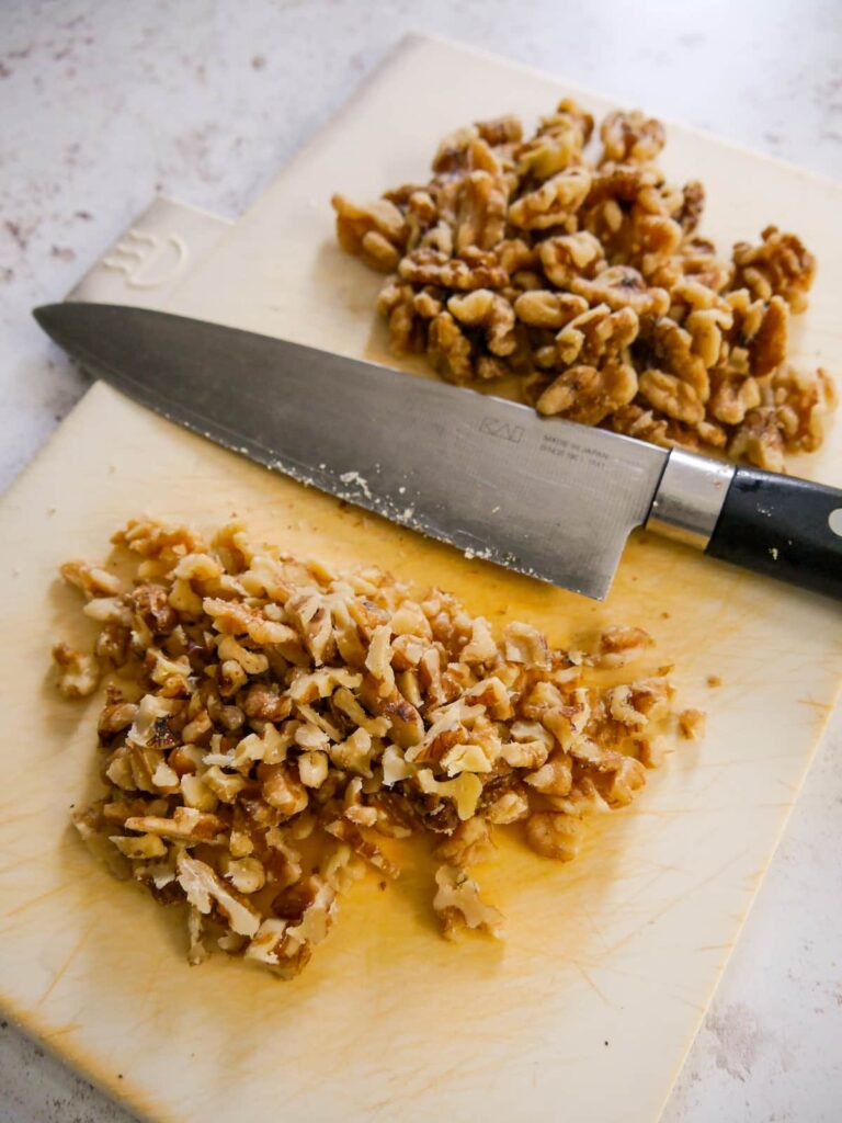 A chopping board with walnuts and a pile of chopped walnuts.