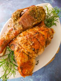 Roasted turkey drumstick and thigh set on a white plate garnished with sprigs of fresh rosemary.