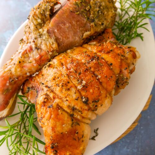 Roasted turkey drumstick and thigh set on a white plate garnished with sprigs of fresh rosemary.