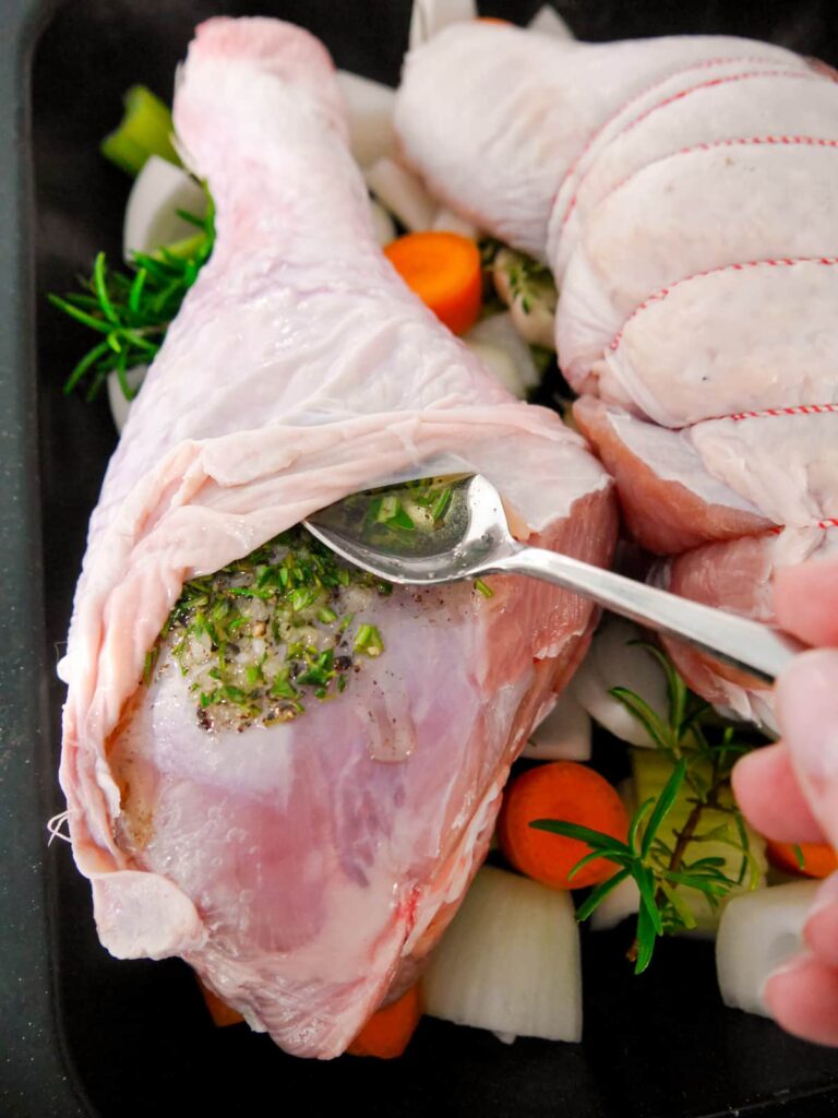 A turkey drumstick with the skin pushed back with rosemary and thyme infused olive oil being added.