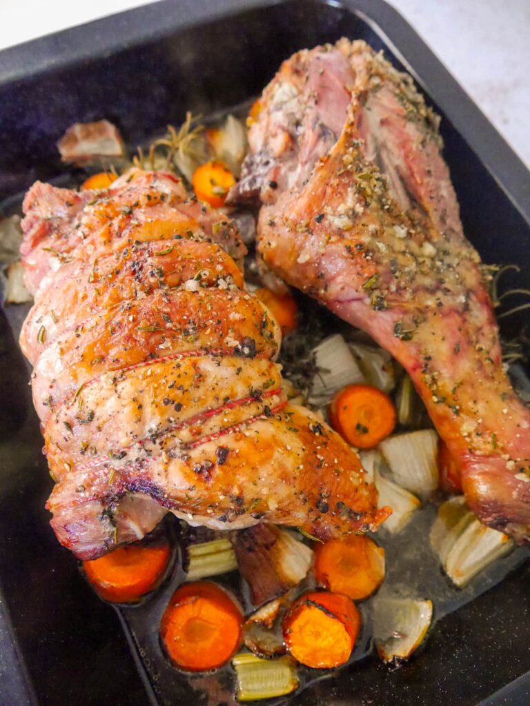 A roasting dish with roasted turkey drumstick and thigh set on top of vegetables.