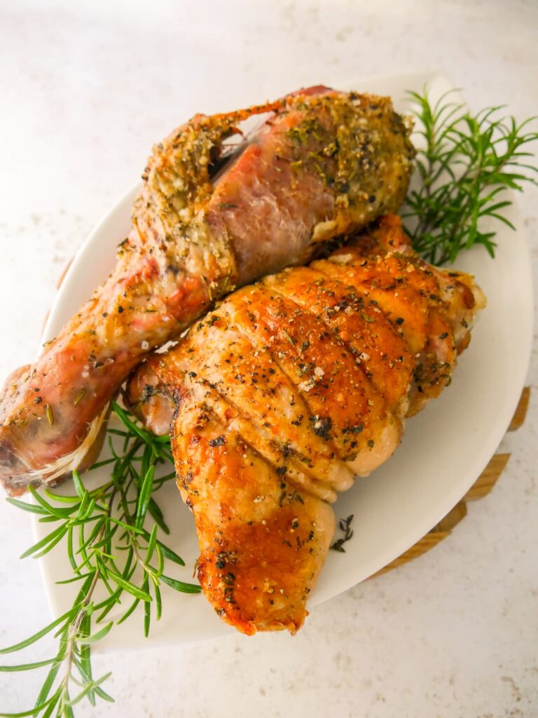 Roasted turkey drumstick and thigh set on a white plate garnished with sprigs of fresh rosemary.