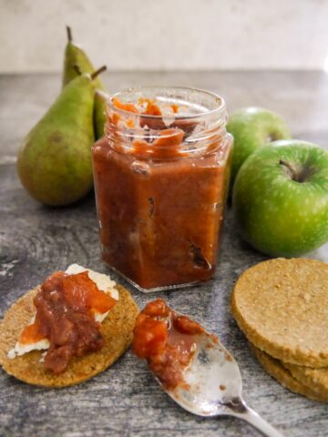 A jar of spiced pear and apple chutney with pears, apples and oatcakes topped with cheese and chutney set alongside.