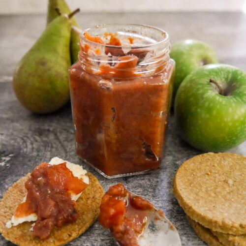 A jar of spiced pear and apple chutney with pears, apples and oatcakes topped with cheese and chutney set alongside.