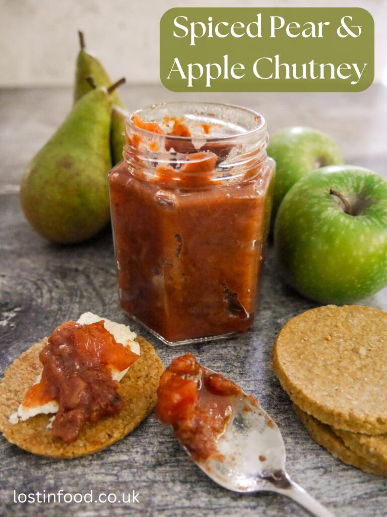 Pinnable image with recipe title and a jar of spiced pear and apple chutney with pears, apples and oatcakes topped with cheese and chutney set alongside.