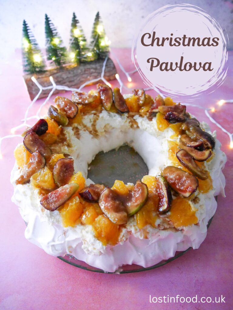 Pinnable image with recipe title and a Christmas pavlova wreath topped with fresh orange segments and warm figs and syrup.