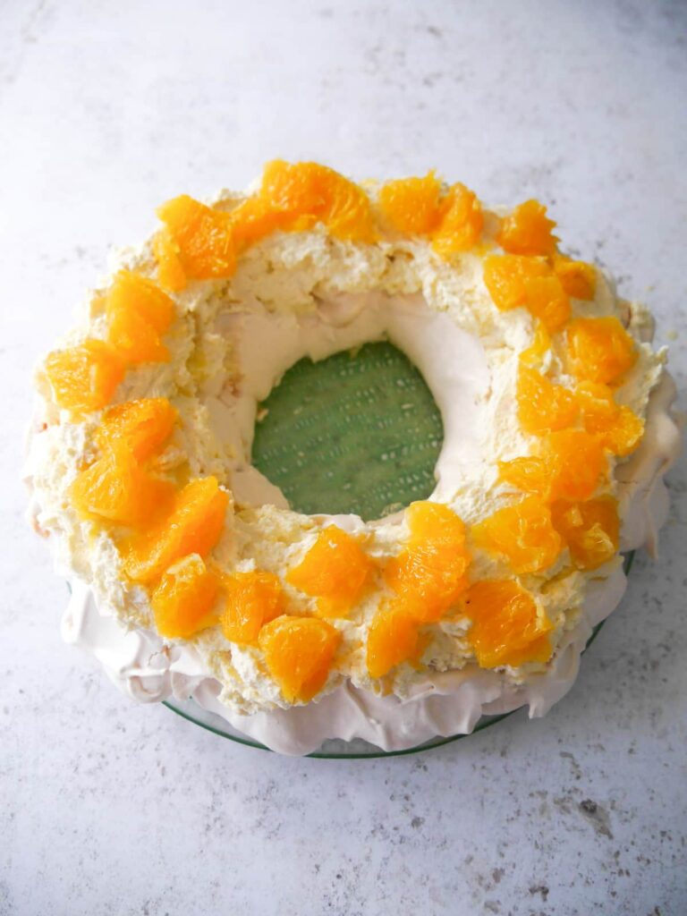 Christmas pavlova meringue wreath topped with whipped ginger cream and orange segments.