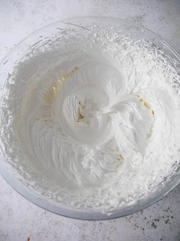 A bowl of whipped egg whites with added sugar and vinegar to form a meringue mixture.