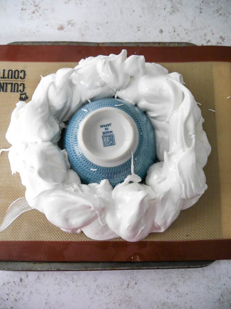 A lined baking sheet with a ring of whipped meringue set out around a small bowl.