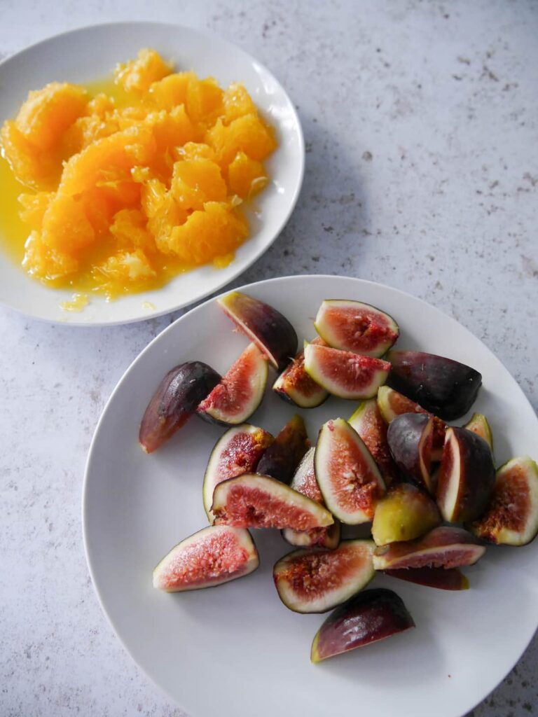 A plate with fresh orange cut into small segments, and a further plate with quartered fresh figs.