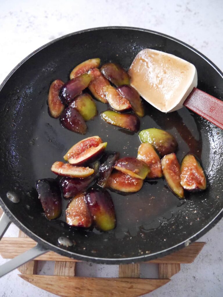 A skillet of fresh fig quarters being softened in a syrup.