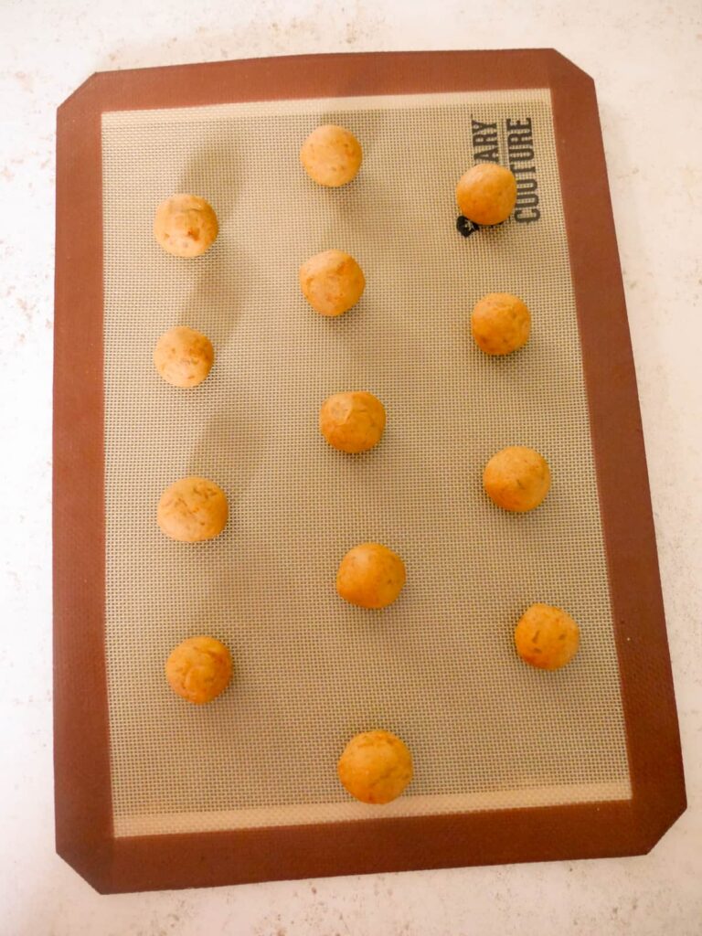 Balls of raw cookie dough set onto a baking sheet topped with a silicone mat.