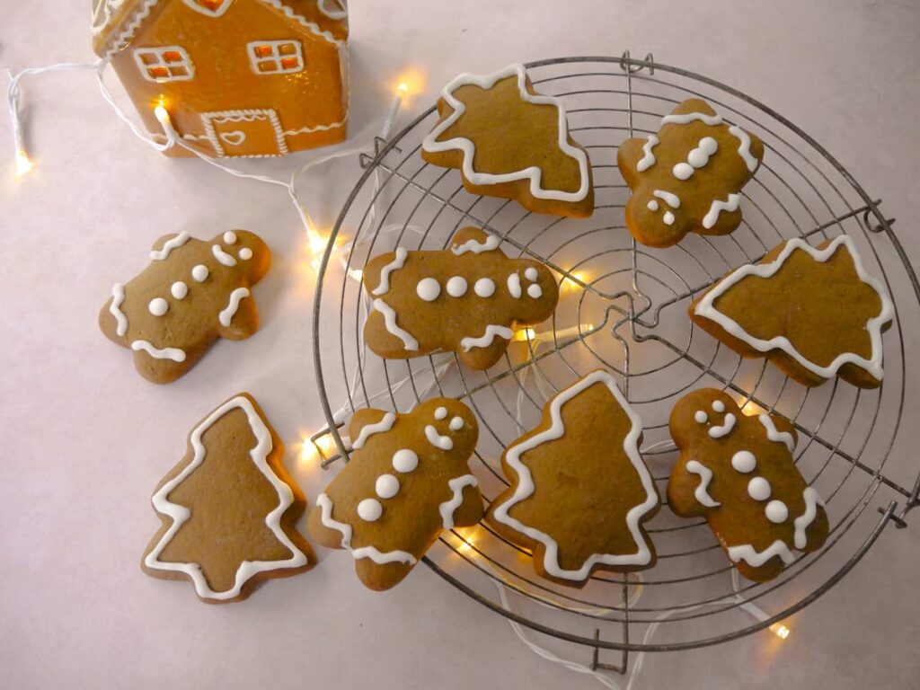 A wire tray of spiced Christmas cookies in the shape of gingerbread men and Christmas trees, decorated with icing.