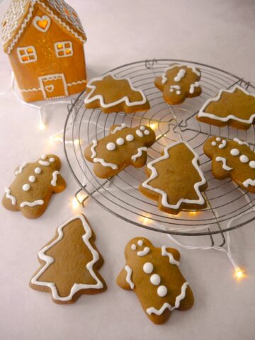 A wire tray of spiced Christmas cookies in the shape of gingerbread men and Christmas trees, decorated with icing.