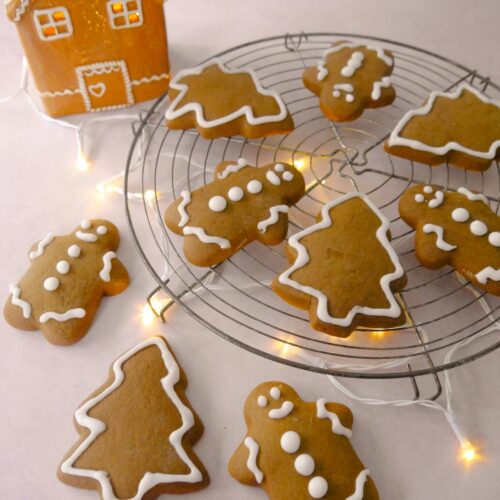 A wire tray of spiced Christmas cookies in the shape of gingerbread men and Christmas trees, decorated with icing.