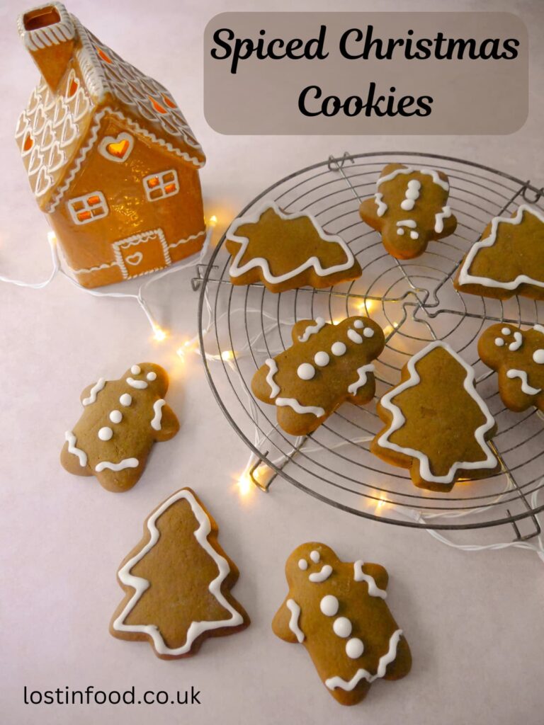 Pinnable image with recipe title and a wire tray of spiced Christmas cookies in the shape of gingerbread men and Christmas trees, decorated with icing.